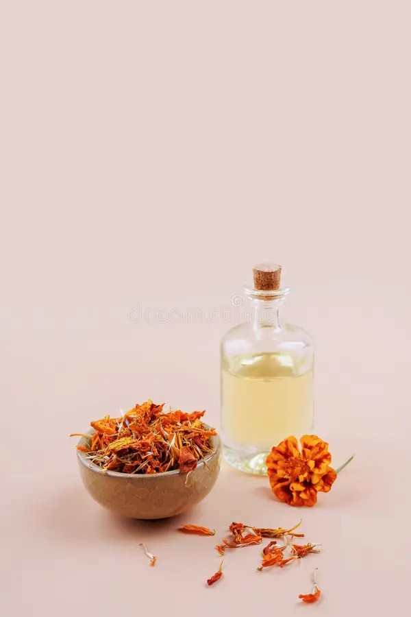 Mangkuk keramik tradisional berisi air rendaman kelopak bunga asoka segar dan botol kaca minyak atsiri herba alami.